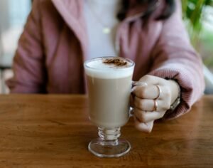 Person holding a glass of latte macchiato on a wooden table indoors.