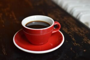 Aromatic black coffee in a red ceramic cup and saucer on a rustic wooden table, perfect for breakfast.