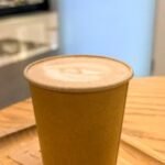 A warm cafe setting featuring a cappuccino and a brigadeiro on a wooden tray.
