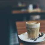 A latte with heart-shaped foam art on a wooden table in a cozy café setting.