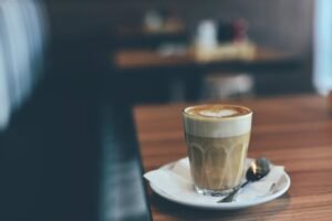 A latte with heart-shaped foam art on a wooden table in a cozy café setting.